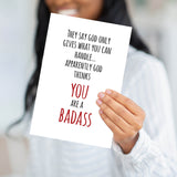 Close-up of a person holding the God Thinks You Are a Badass card, showing the sturdy 320 GSM paper.